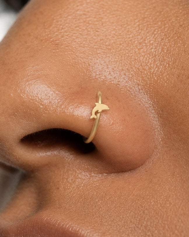 Bring a little of the sea to your everyday jewellery. This 14ct solid gold dolphin nostril ring pairs an approximately 3mm polished dolphin silhouette with a smooth seamless hoop. Its curved body, small fins and forked tail create a playful ocean-inspired detail.
Handmade to order in yellow, white or rose gold, with inner diameters from 6 to 10mm and a choice of 18G (1.0mm) or 20G (0.8mm). Both the dolphin and hoop are solid gold and nickel-free, designed for a fully healed nostril piercing.
Wear it alone f