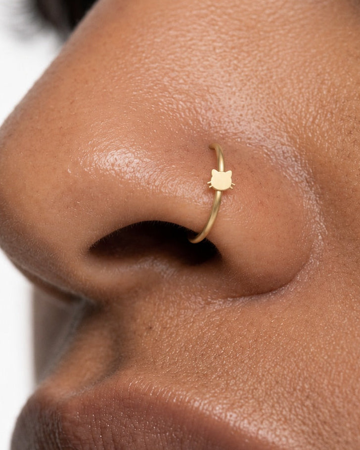 Two little ears and a few whiskers give this hoop its feline character. This 14ct solid gold cat head nostril ring pairs an approximately 3mm polished cat-face silhouette with a smooth seamless hoop. The rounded face is left plain, allowing the ears and whiskers to define the design.
Handmade to order in yellow, white or rose gold, with inner diameters from 6 to 10mm and a choice of 18G (1.0mm) or 20G (0.8mm). Both the cat head and hoop are solid gold and nickel-free, designed for a fully healed nostril pie