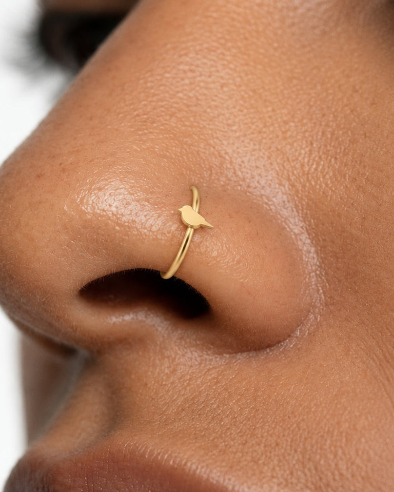 A little bird for your everyday jewellery. This 14ct solid gold bird nostril ring pairs an approximately 3mm polished bird silhouette with a smooth seamless hoop. A rounded head and breast, small pointed beak and tapered tail define the design, with no engraved feather pattern or gemstones.
Handmade to order in yellow, white or rose gold, with inner diameters from 6 to 10mm and a choice of 18G (1.0mm) or 20G (0.8mm). Both the bird and hoop are solid gold and nickel-free, designed for a fully healed nostril 