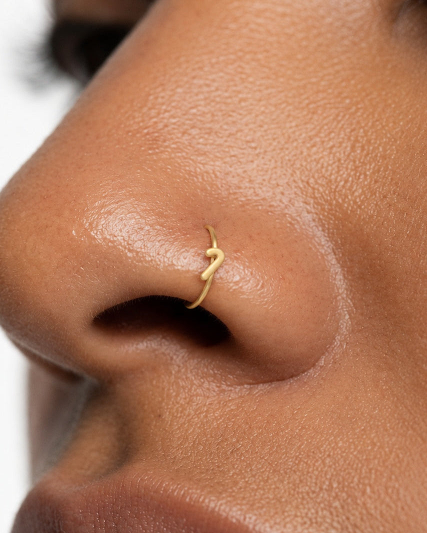 This miniature candy cane has a curved hook at the top and a straight stem with a rounded end. Its smooth gold surface has no engraved stripes, coloured enamel or gemstones, keeping the Christmas sweet-inspired outline clear and minimal.

Handmade to order in nickel-free 14ct solid gold, this candy cane nostril hoop is available in yellow, white or rose gold. Choose a 6, 7, 8, 9 or 10mm internal diameter and 18G (1.0mm) or 20G (0.8mm). The motif measures approximately 3mm. Designed for fully healed nostril 