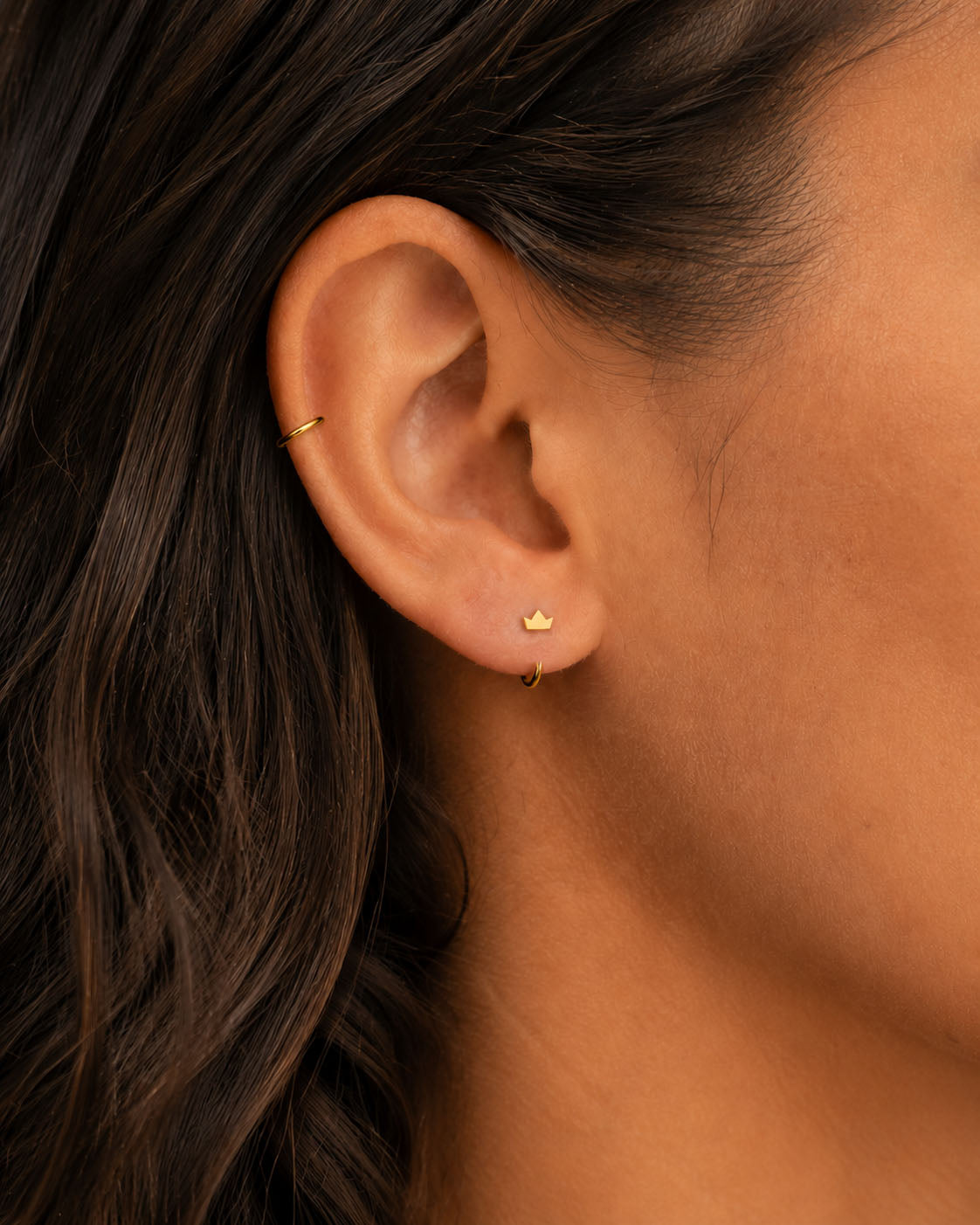 A distinctive 14ct solid gold crown huggie hoop with an open design for easier fitting. No twisting or end alignment required — simply guide the smooth end through your fully healed nose or ear piercing and rotate it into position.