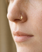 This miniature snowman wears a top hat and has a rounded body with two outstretched, twig-like arms. Its smooth gold surface has no engraved eyes, buttons or gemstones, keeping the winter silhouette simple and clear.

Handmade to order in nickel-free 14ct solid gold, this snowman nostril hoop is available in yellow, white or rose gold. Choose a 6, 7, 8, 9 or 10mm internal diameter and 18G (1.0mm) or 20G (0.8mm). The motif measures approximately 3mm. Designed for fully healed nostril piercings, with sizing c