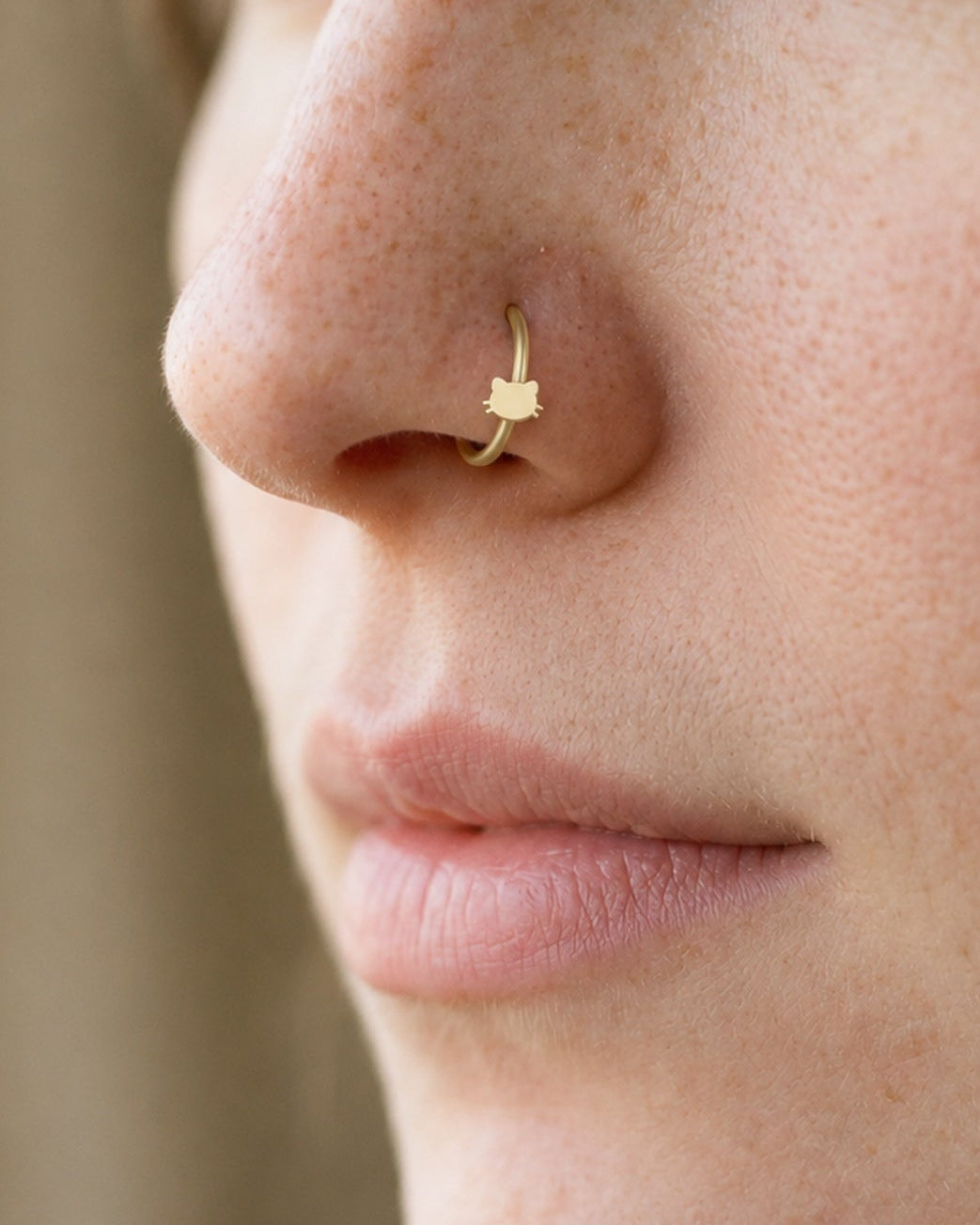 Two little ears and a few whiskers give this hoop its feline character. This 14ct solid gold cat head nostril ring pairs an approximately 3mm polished cat-face silhouette with a smooth seamless hoop. The rounded face is left plain, allowing the ears and whiskers to define the design.
Handmade to order in yellow, white or rose gold, with inner diameters from 6 to 10mm and a choice of 18G (1.0mm) or 20G (0.8mm). Both the cat head and hoop are solid gold and nickel-free, designed for a fully healed nostril pie