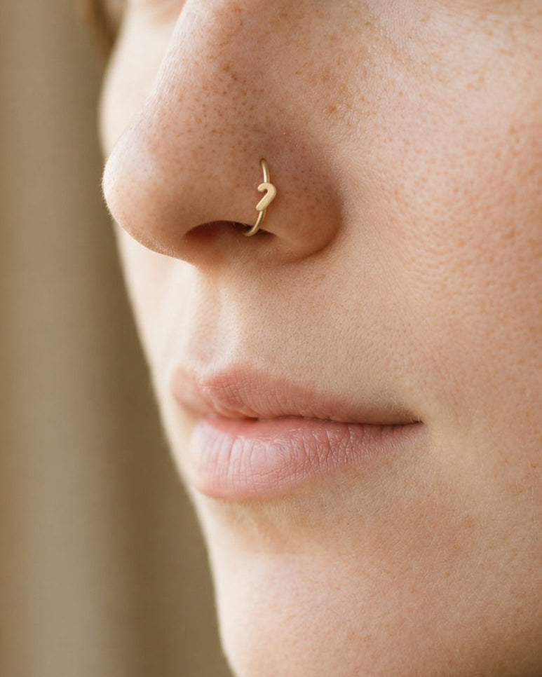This miniature candy cane has a curved hook at the top and a straight stem with a rounded end. Its smooth gold surface has no engraved stripes, coloured enamel or gemstones, keeping the Christmas sweet-inspired outline clear and minimal.

Handmade to order in nickel-free 14ct solid gold, this candy cane nostril hoop is available in yellow, white or rose gold. Choose a 6, 7, 8, 9 or 10mm internal diameter and 18G (1.0mm) or 20G (0.8mm). The motif measures approximately 3mm. Designed for fully healed nostril 