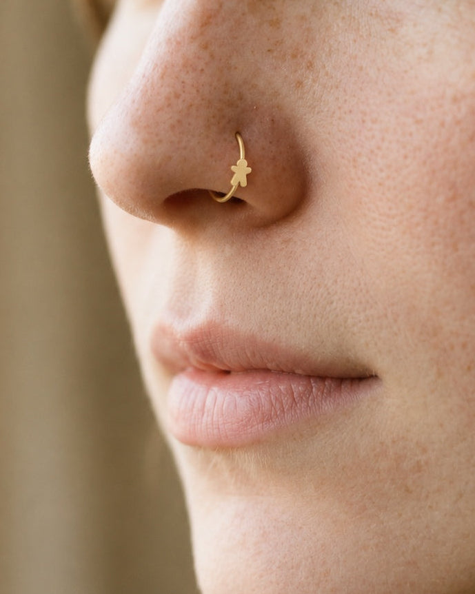 This miniature gingerbread man has a round head, two outstretched arms and two separated legs with rounded ends. Its smooth gold surface has no engraved face, buttons or icing patterns, keeping the classic Christmas biscuit silhouette simple and clear.

Handmade to order in nickel-free 14ct solid gold, this gingerbread man nostril hoop is available in yellow, white or rose gold. Choose a 6, 7, 8, 9 or 10mm internal diameter and 18G (1.0mm) or 20G (0.8mm). The motif measures approximately 3mm. Designed for f