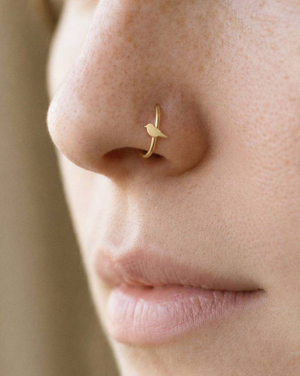 A little bird for your everyday jewellery. This 14ct solid gold bird nostril ring pairs an approximately 3mm polished bird silhouette with a smooth seamless hoop. A rounded head and breast, small pointed beak and tapered tail define the design, with no engraved feather pattern or gemstones.
Handmade to order in yellow, white or rose gold, with inner diameters from 6 to 10mm and a choice of 18G (1.0mm) or 20G (0.8mm). Both the bird and hoop are solid gold and nickel-free, designed for a fully healed nostril 