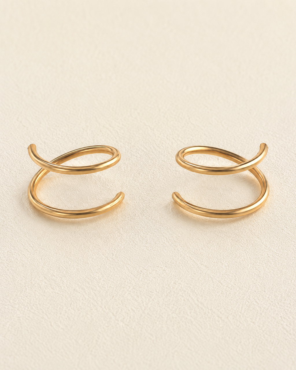 A pair of 14k solid gold doble hoop nose ring with a twisted, looped design, displayed on a textured cream-colored surface. left and right side 