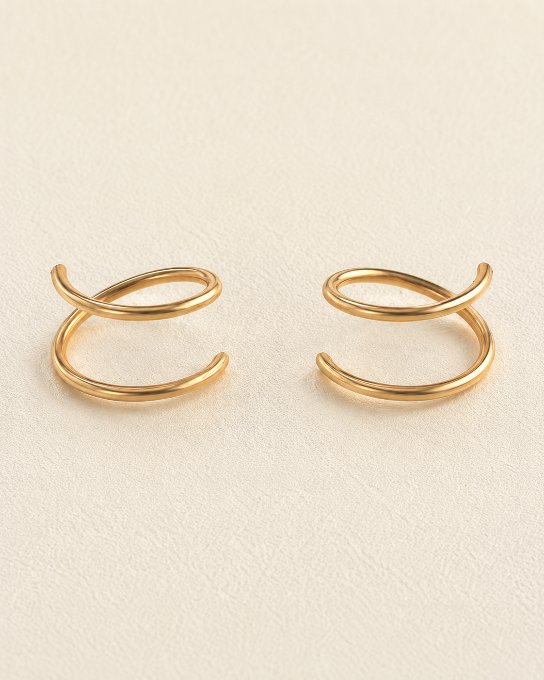 A pair of 14k solid gold doble hoop nose ring with a twisted, looped design, displayed on a textured cream-colored surface. left and right side 