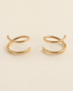 A pair of 14k solid gold doble hoop nose ring with a twisted, looped design, displayed on a textured cream-colored surface. left and right side 