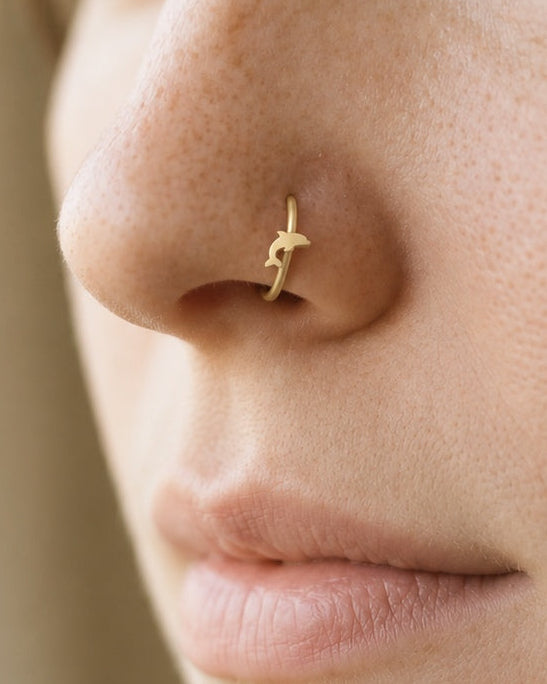 Bring a little of the sea to your everyday jewellery. This 14ct solid gold dolphin nostril ring pairs an approximately 3mm polished dolphin silhouette with a smooth seamless hoop. Its curved body, small fins and forked tail create a playful ocean-inspired detail.
Handmade to order in yellow, white or rose gold, with inner diameters from 6 to 10mm and a choice of 18G (1.0mm) or 20G (0.8mm). Both the dolphin and hoop are solid gold and nickel-free, designed for a fully healed nostril piercing.
Wear it alone f